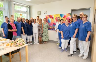 Gruppenbild des Teams der Sektion Altersmedizin. Im Hintergrund ist ein großes, buntes Poster mit einer „10“ zu sehen – aufgenommen bei einer kleinen Feier auf der Station zum 10-jährigen Jubiläum.