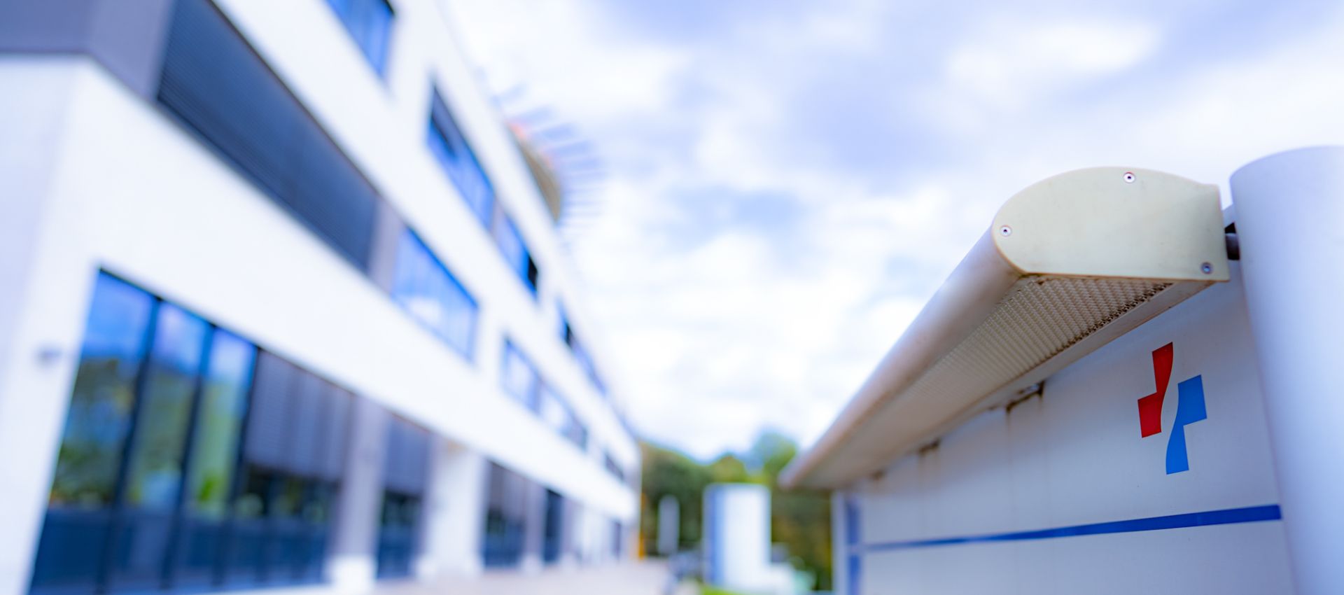 Seitliche Ansicht des Verwaltungsgebäudes am Ev. Krankenhaus Duisburg-Nord mit Blick auf den Weg zur Pflegeschule. Im Vordergrund ist ein weißes Schild mit dem Logo des Verbunds zu sehen. Der Himmel ist leicht bewölkt.