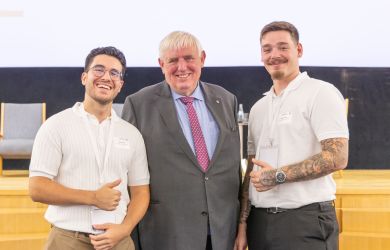 Gruppenfoto beim Fachtag „Zukunftsbündnis Pflege“: In der Mitte NRW-Gesundheitsminister Karl-Josef Laumann, flankiert von zwei jungen Pflegeauszubildenden in weißem Poloshirt. Alle drei lächeln, im Hintergrund eine Bühne mit Leinwand.
