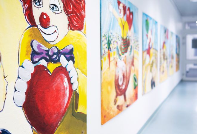 Heller, freundlicher Stationsflur der Kinderkardiologie. An der linken Wand hängen mehrere bunte, gemalte Bilder mit Clown-Motiven.