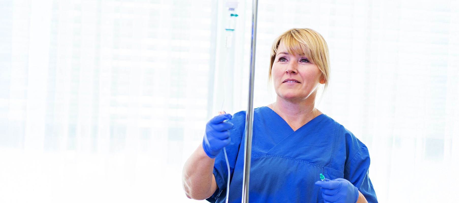 Eine weibliche Pflegekraft bereitet eine Infusion vor, die sie gleich an einen Patienten anschließen möchte.
