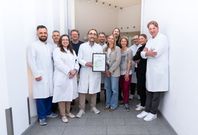 Mehrere Mitarbeitende des Lungenkrebszentrums Johanniter Krankenhaus Oberhausen Niederrhein stehen für ein Gruppenfoto in einem hellen Klinikflur zusammen. Eine Person in der Mitte hält die Zertifizierungsurkunde.