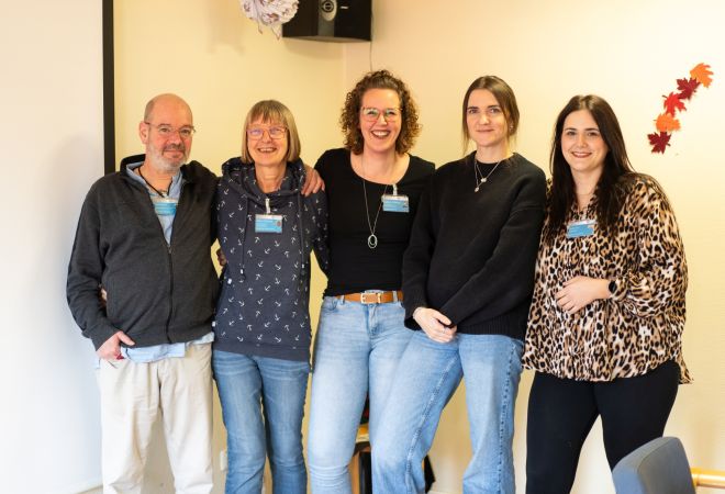 Ein Mitarbeiter und vier Mitarbeiterinnen der Tagespflege Oberhausen Sterkrade stehen nebeneinander, lächeln in die Kamera und posieren gemeinsam für ein Gruppenfoto.