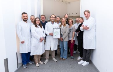 Mehrere Mitarbeitende des Lungenkrebszentrums Johanniter Krankenhaus Oberhausen Niederrhein stehen für ein Gruppenfoto in einem hellen Klinikflur zusammen. Eine Person in der Mitte hält die Zertifizierungsurkunde.