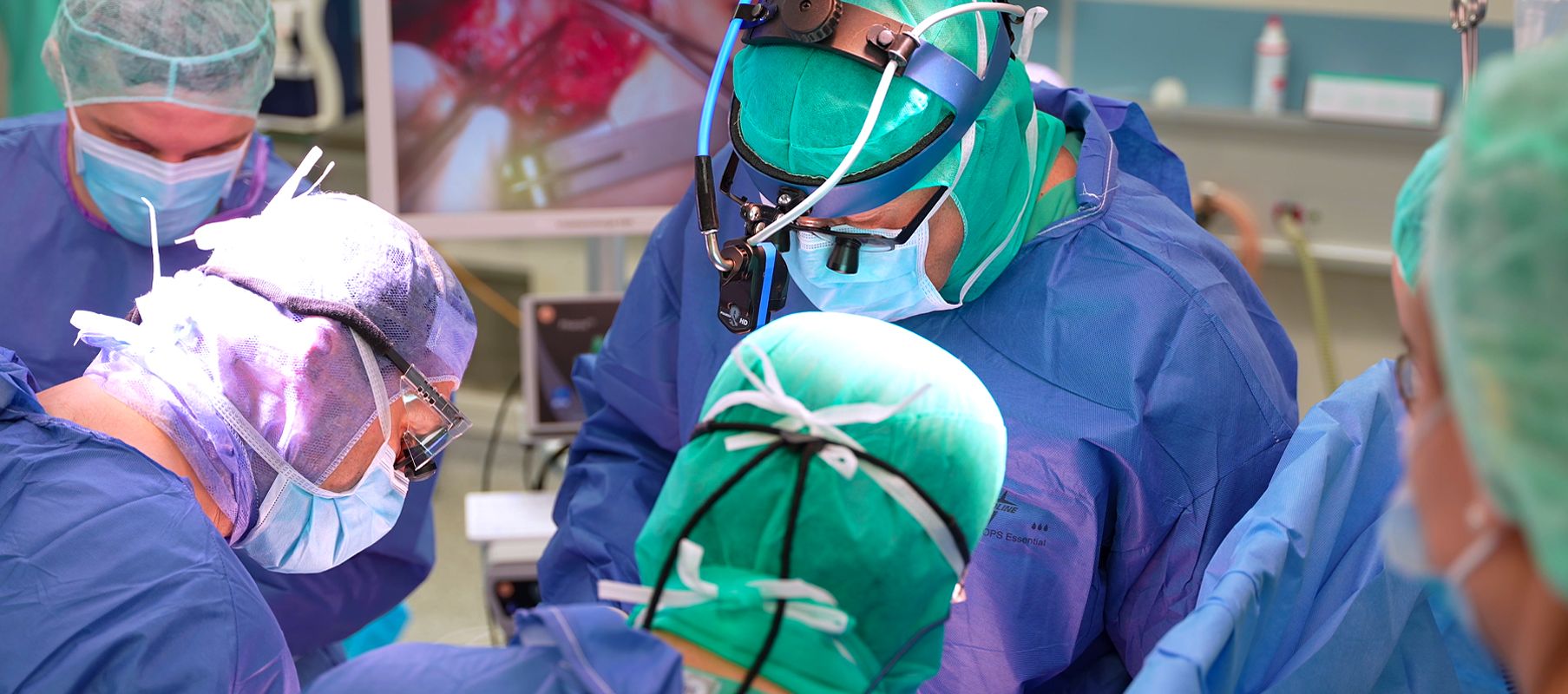 Dr. Scheid operiert gemeinsam mit seinem Team ein Kind am offenen Herzen und trägt dabei ein spezielles Operationsmikroskop.