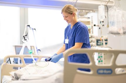 Eine weibliche Pflegefachkraft auf der Intensivstation überprüft den Cuffdruck eines Beatmungsschlauchs an einem Patientenbett, um eine sichere Belüftung zu gewährleisten.
