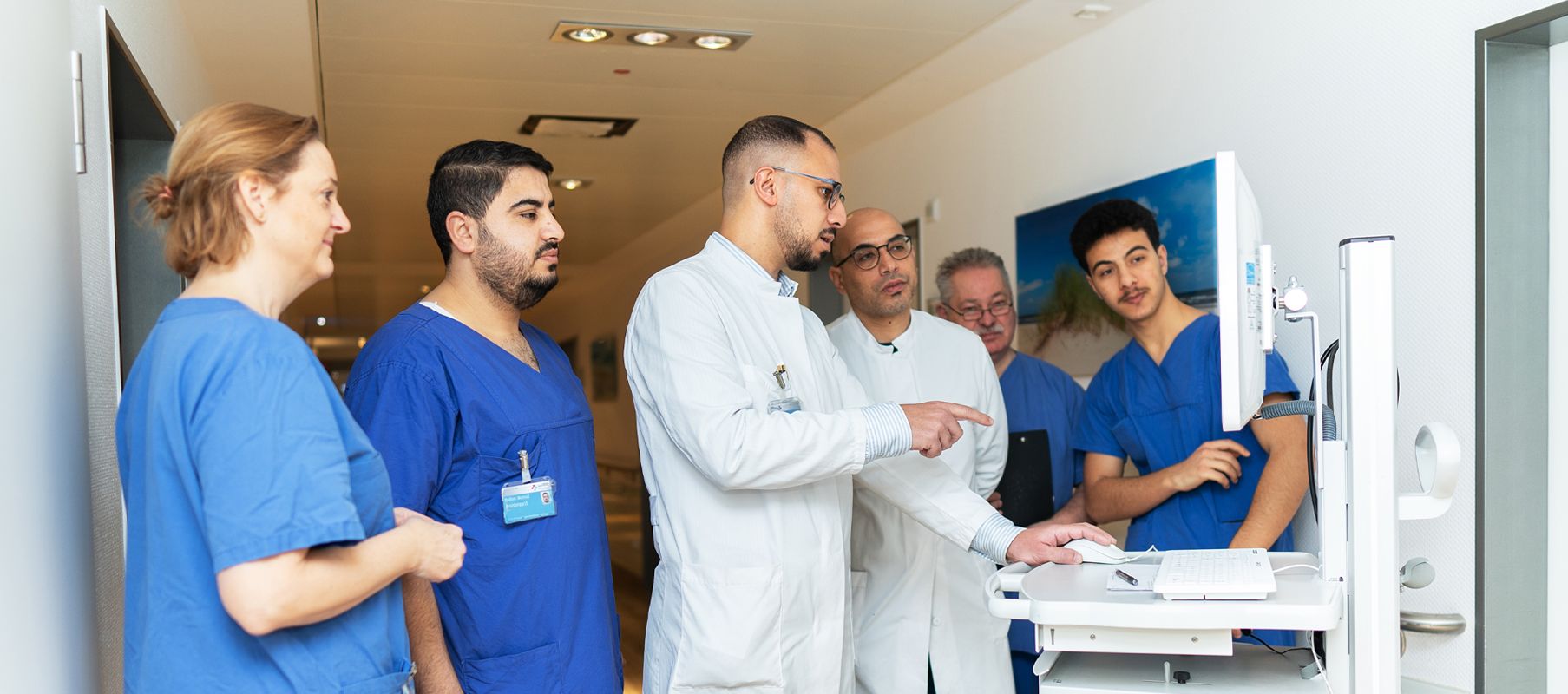 Das Team um Hr. Alsingaby steht vor einer digitalen mobilen Dokumentationseinheit. Hr. Alsingaby zeigt auf den Monitor und erklärt etwas.