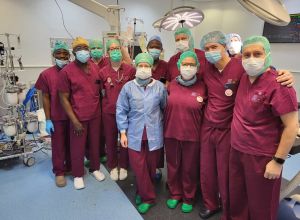 Gruppenfoto der Teams des Herzzentrums Duisburg und des University of Ghana Medical Center im OP-Saal nach einem Eingriff. Alle Personen tragen weinrote OP-Kleidung, grüne Hauben und medizinische Masken.