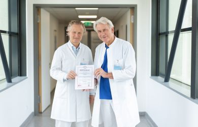 Prof. Dr. Jochen Börgermann und Prof. Dr. Wolfgang Schöls halten gemeinmsan die Urkunde der Zertifizierung hoch.