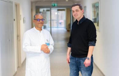 Der Patient Dino Andree Rogge steht gemeinsam mit Dr. Rashad El-Habony, leitender Oberarzt der Neurochirurgie, in einem hellen Klinikflur des Evangelischen Klinikums Niederrhein. Beide blicken in die Kamera und lächeln.