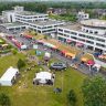 Vogelperspektive auf das Klinikgelände während des Tags der offenen Tür: Im Bild das Krankenhaus- und Verwaltungsgebäude, davor eine Wiese mit Pavillons, Info- und Aktionsständen sowie Gastronomiewagen, umgeben von Besucherinnen und Besuchern.