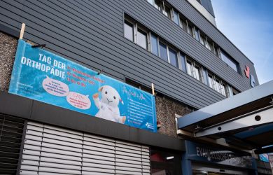 Außenaufnahme des Evangelischen Krankenhauses Dinslaken mit großem Banner zum "Tag der Orthopädie" am 22. November 2025. Zu sehen ist Maskottchen Eva auf blauem Hintergrund mit Veranstaltungsinfos.