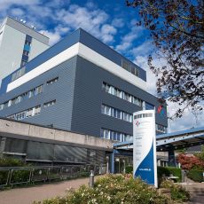 Vor dem Haupteingang des Evangelischen Krankenhauses Dinslaken ist ein barrierefreier Weg und eine Treppe. Ein Schild mit dem Namen des Krankenhauses und des Klinikverbundes ist sichtbar.