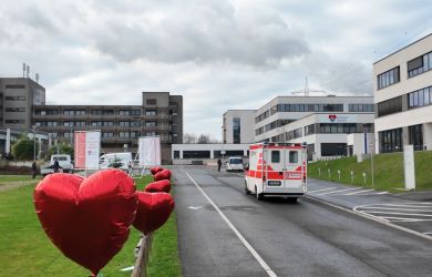 Blick auf die Einfahrt zum Krankenhaus. Am Zaun links sind große, rote Herzballons befestigt. Rechts steht ein RTW. Im Hintergrund ist das Klinikgebäude zu sehen.