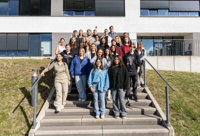 Gruppenfoto mit 26 Auszubildenden und einem Lehrer. Die Gruppe steht auf der Treppe vor dem Verwaltungsgebäude des Evangelischen Krankenhauses Duisburg-Nord.