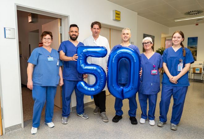 Ein Team aus Ärztinnen, Ärzten und Pflegekräften steht im Klinikflur zusammen und hält große blaue Luftballons in Form der Zahl 50. Das Foto entstand anlässlich der 50. Kryoablation am Johanniter Krankenhaus Oberhausen.