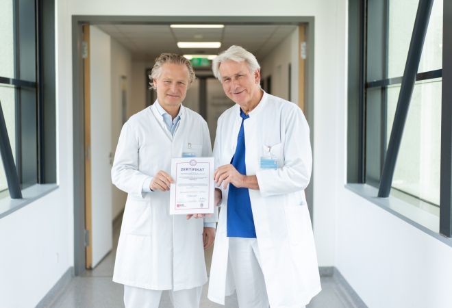 Prof. Dr. Jochen Börgermann und Prof. Dr. Wolfgang Schöls halten gemeinmsan die Urkunde der Zertifizierung hoch.