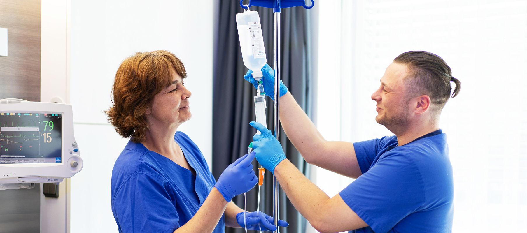 Zwei Pflegekräfte bereiten gemeinsam eine Infusion für den Anschluss an einen Patienten vor. Sie arbeiten konzentriert und stimmen sich dabei miteinander ab.