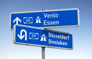Zwei blaue Autobahnschilder mit weißen Richtungspfeilen. Auf einem steht „40 Venlo Essen“, auf dem anderen „59 Dinslaken Duisburg“. Die Schilder symbolisieren die Lage im westlichen Ruhrgebiet.