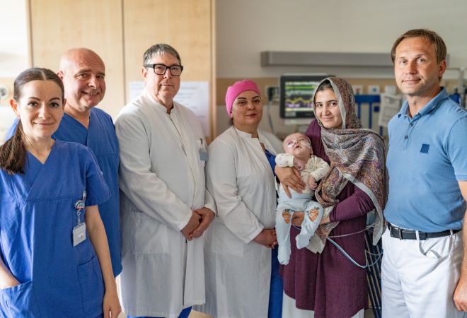 Gruppenfoto auf einer Station im Kimderherzzentrum: Sechs Personen stehen nebeneinander. Von links nach rechts: eine Stationsleiterin, zwei Chefärzte, eine Neurochirurgin, die Mutter mit dem Kind sowie ein Herzchirurg.