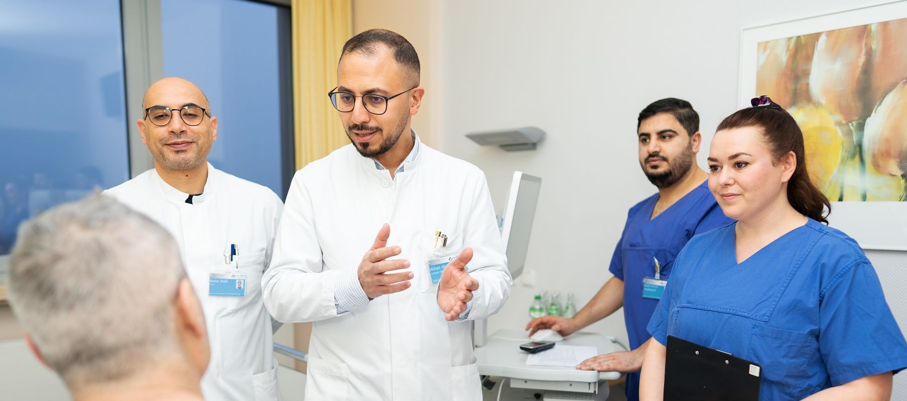Hr. Alsingaby steht im Zimmer vor einem Patienten und erklärt die Therapie. Mit anwesend ist sein Team.