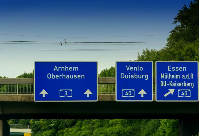 Drei blaue Autobahnschilder mit weißen Richtungspfeilen hängen an einer Brücke. Auf einem steht „3 Arnhem Oberhausen“, die anderen verweisen auf die A40 Venlo Duisburg und A40 Essen, Mülheim an der Ruhr und DU-Kaiserberg.