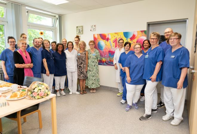 Gruppenbild des Teams der Sektion Altersmedizin. Im Hintergrund ist ein großes, buntes Poster mit einer „10“ zu sehen – aufgenommen bei einer kleinen Feier auf der Station zum 10-jährigen Jubiläum.