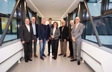Gruppenbild des Aufsichtsrats des Evangelischen Klinikums Niederrhein, aufgenommen im Übergang zwischen zwei Gebäudeteilen mit Fensterfronten.