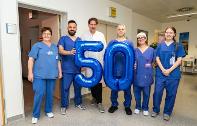 Ein Team aus Ärztinnen, Ärzten und Pflegekräften steht im Klinikflur zusammen und hält große blaue Luftballons in Form der Zahl 50. Das Foto entstand anlässlich der 50. Kryoablation am Johanniter Krankenhaus Oberhausen.