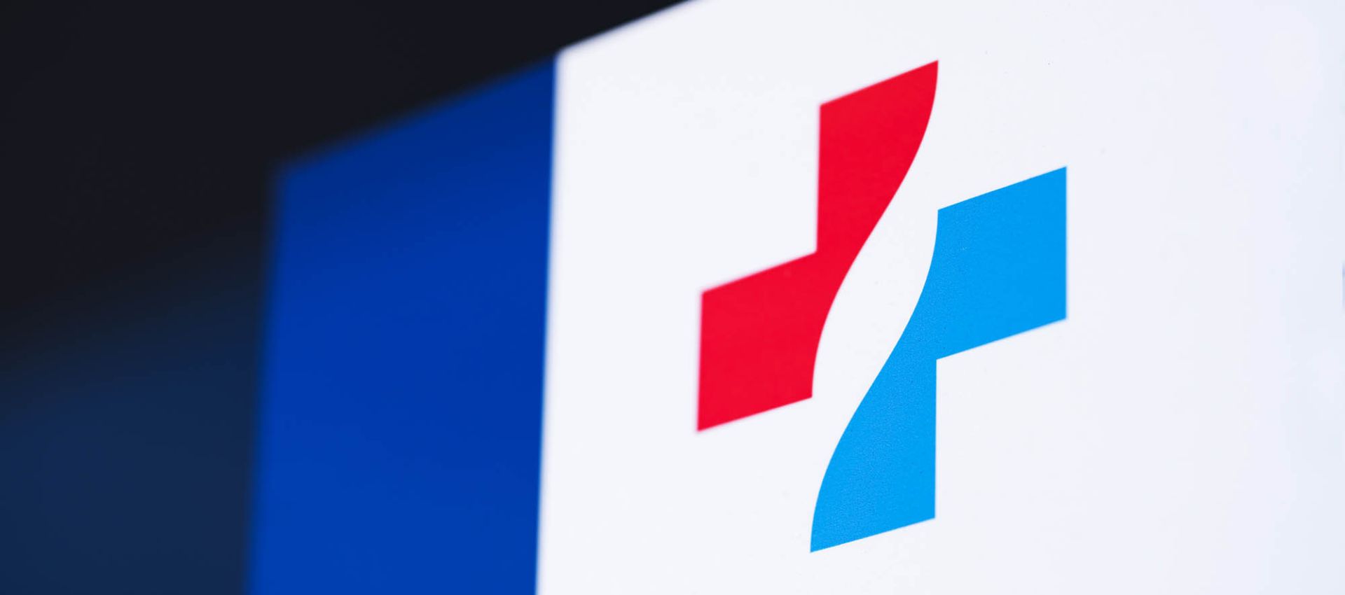 Das Logo des Klinikverbundes, ein rot-blaues Kreuz, ist groß auf einer Glasfläche sichtbar angebracht.