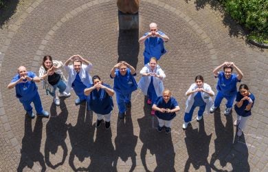 Das Team der Elektrophysiologie freut sich über die Zertifizierung. Es steht draußen vor dem Herzzentrum auf einer Kreide-EKG-Linie, die einen gesunden Herzrhythmus darstellt.